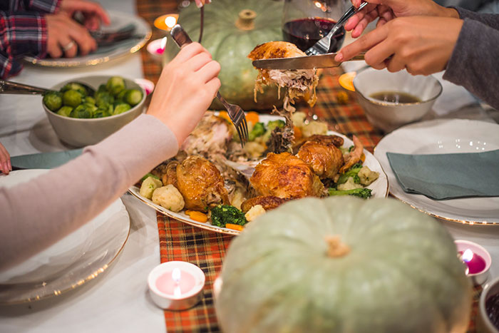 Family serving roasted turkey and vegetables at a Thanksgiving dinner table, highlighting refusing to bring expensive food.