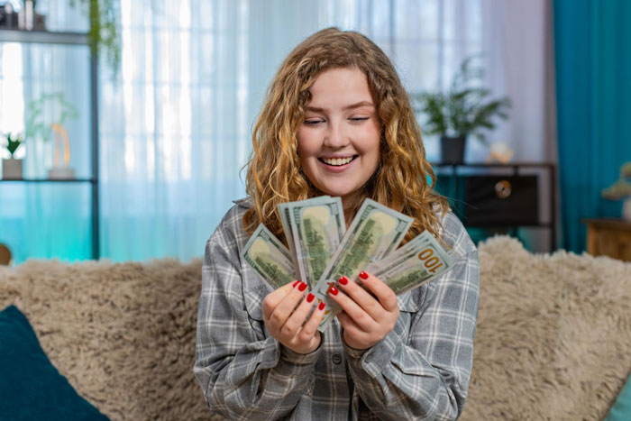 Young woman smiling at cash in hand, representing 18YO planning to spend grandpa's inheritance on a BBL.