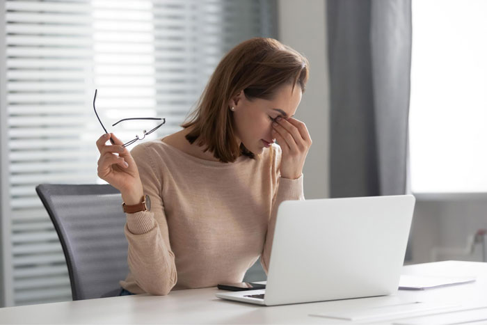Stressed analyst at desk holding glasses and rubbing eyes, illustrating refusal of free labor and workplace conflict.