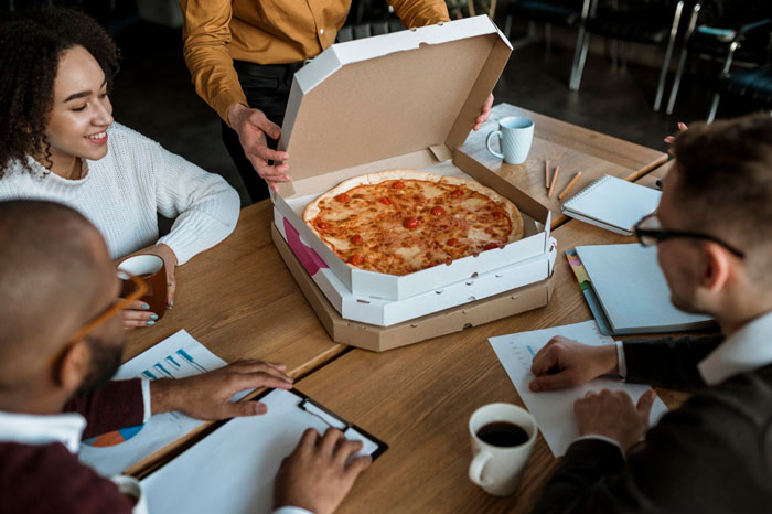 Team of analysts at a meeting with snacks and pizza, highlighting office culture and party planning conflicts.