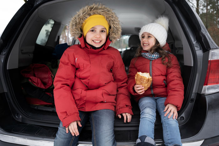 Two children in winter jackets sitting in the back of a car representing a happy family after abandonment reunion.