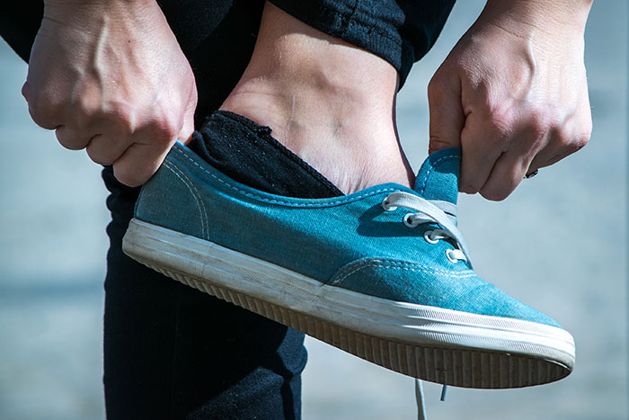 Person putting on a blue sneaker, illustrating lies getting way out of hand and changing lives drastically.