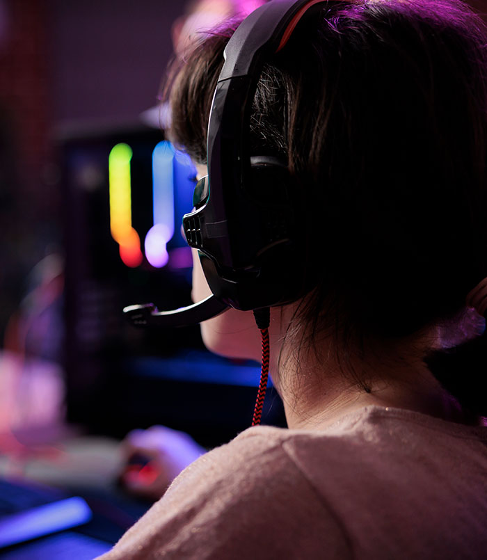 Person wearing gaming headset, focused on computer screen with colorful lights, capturing moments when lies got out of hand.