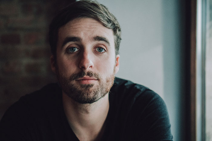 Hombre con expresión sorprendida y pensativa, retrato en interior con luz natural suave reflejando choque emocional.