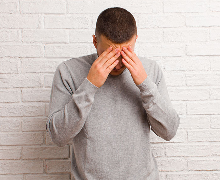 Man in gray sweater covering face with hands, illustrating the impact of people's lies getting out of hand.