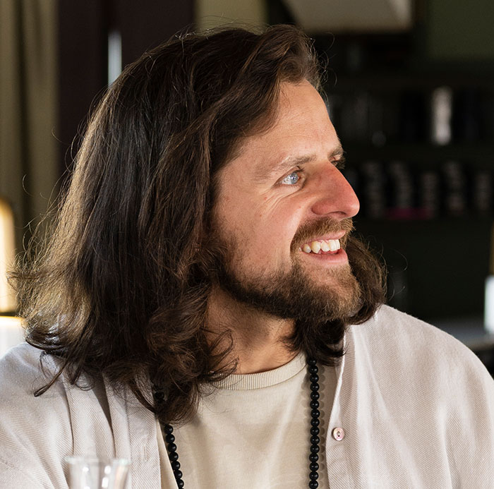Man with long hair and beard smiling indoors, illustrating how people's lies got way out of hand and changed lives.