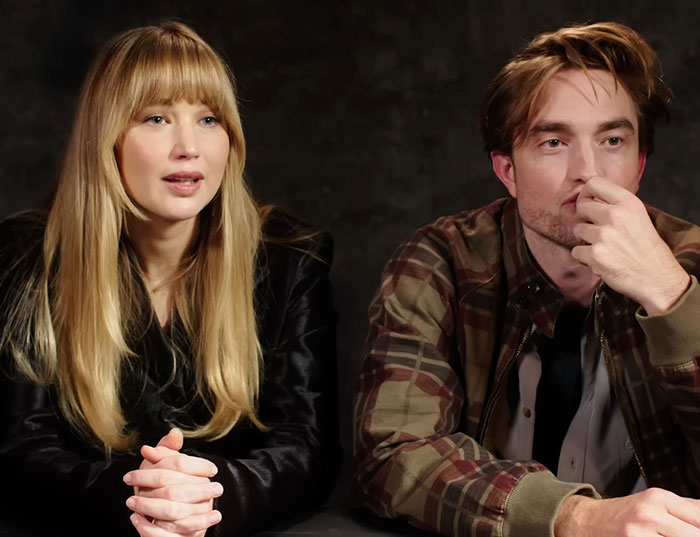 Jennifer Lawrence and Robert Pattinson seated side by side during an interview with neutral expressions