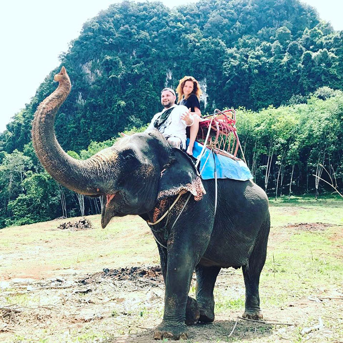 Man and woman riding an elephant in a scenic forest area, related to crypto scammer and Dubai shopping mall incident.