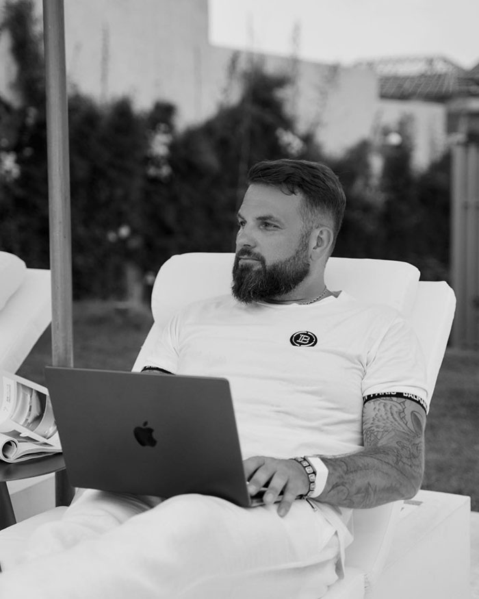 Man with beard working on laptop outdoors, related to crypto scammer behind $500M scheme in Dubai.