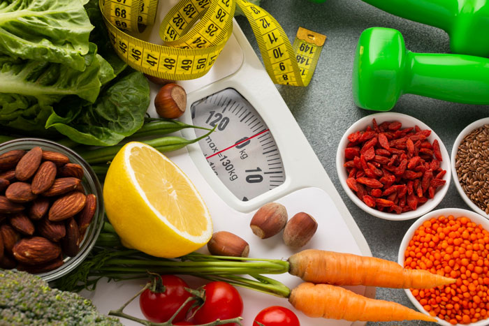 Healthy foods and measuring tape surrounding a weight scale, illustrating strict diet and health nut concepts.