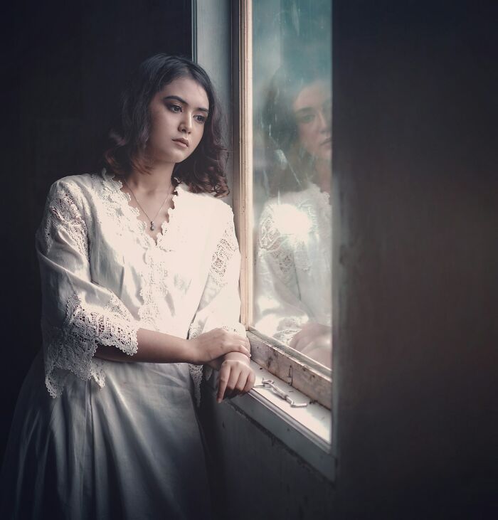 Young woman in a white lace dress looking reflective by a window, illustrating harsh truths about marriage and its reality.
