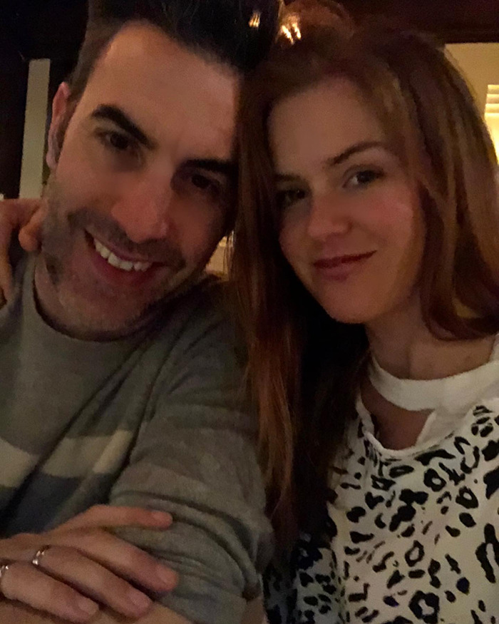 Isla Fisher and Sacha Baron Cohen smiling together in a casual indoor setting following emotional struggle and difficult divorce.