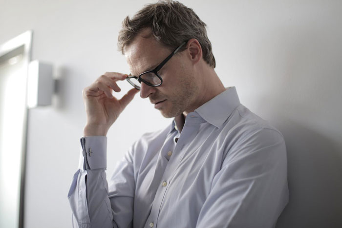 Man in glasses and light shirt looking down with a sad expression, reflecting on stepsister&rsquo;s special needs hospital visit.