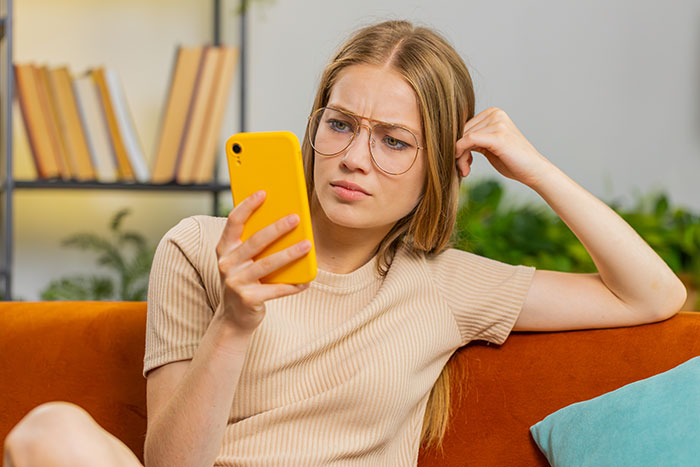 Young woman with glasses looking disappointed at phone, symbolizing boyfriend upgrade after surgery neglect.