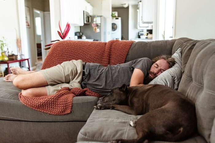 Man and dog resting on couch in a cozy living room, illustrating positive stereotypes of relaxation in various countries.