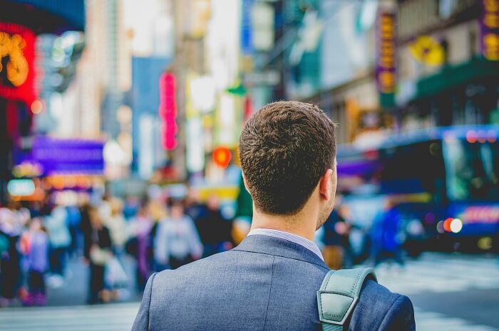 Man in a suit with backpack looking at busy city street representing dilemma of rehoming dog after being abandoned abroad Man in a suit with backpack looking at busy city street representing dilemma of rehoming dog after being abandoned abroad
