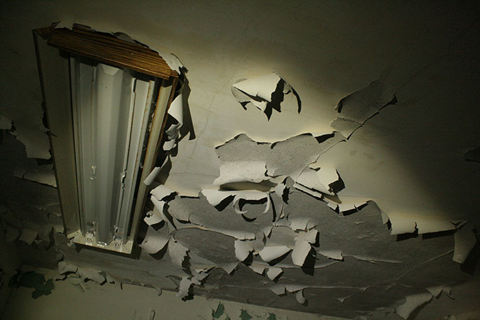 Peeling and damaged ceiling around a broken fluorescent light fixture, evoking a scary and unsettling atmosphere.