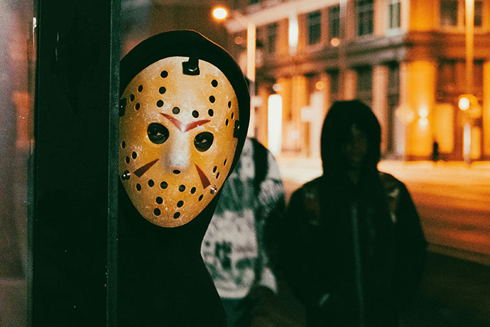 Person wearing a scary mask hiding in shadows at night representing the scariest things people have woken up to