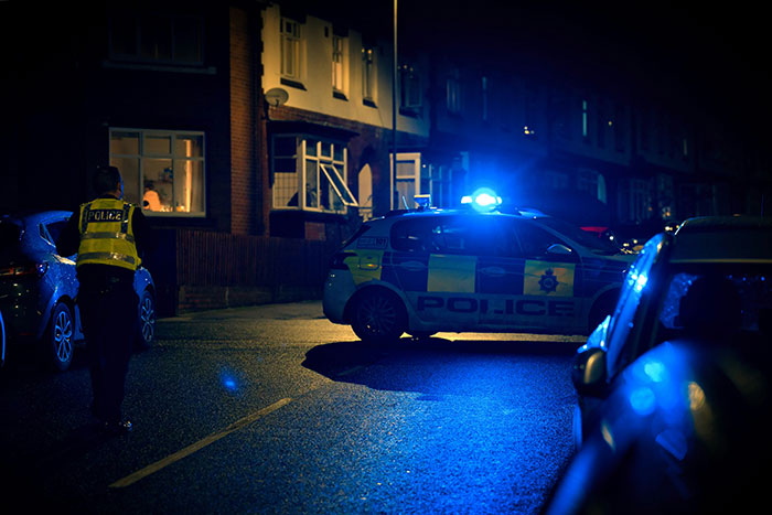 Police car with flashing lights and an officer on a residential street at night, illustrating scariest things people woke up to.