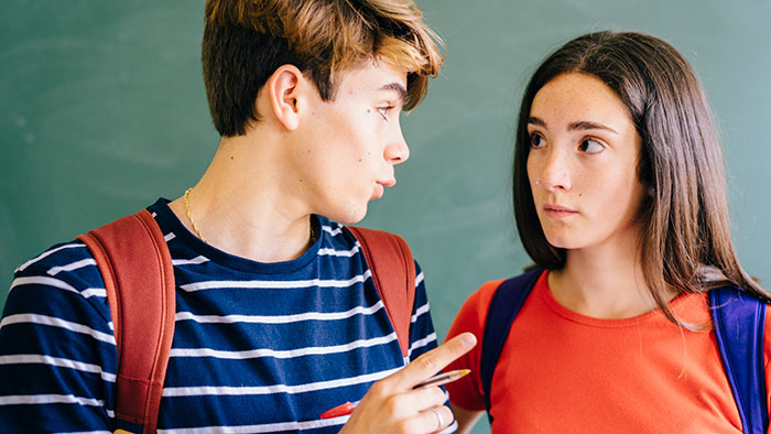 Two classmates having a serious conversation in a classroom, with expressions suggesting drama or tension.