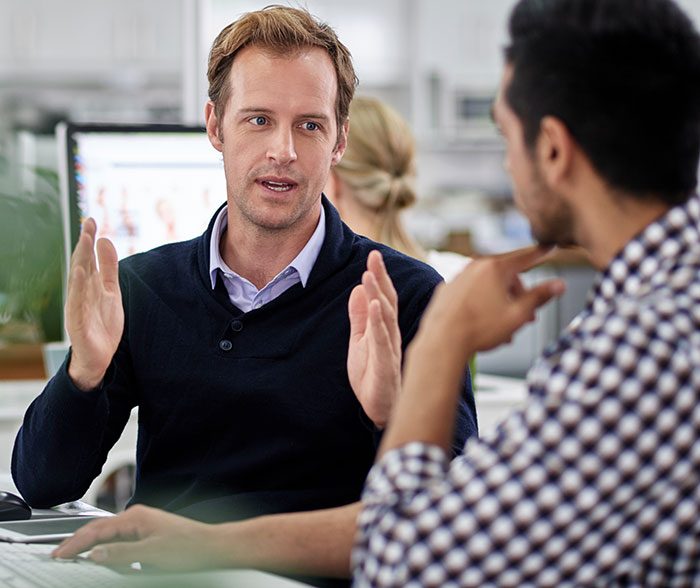 Man explaining Secret Santa organizer rules to coworker in an office setting during a discussion about gift participation.