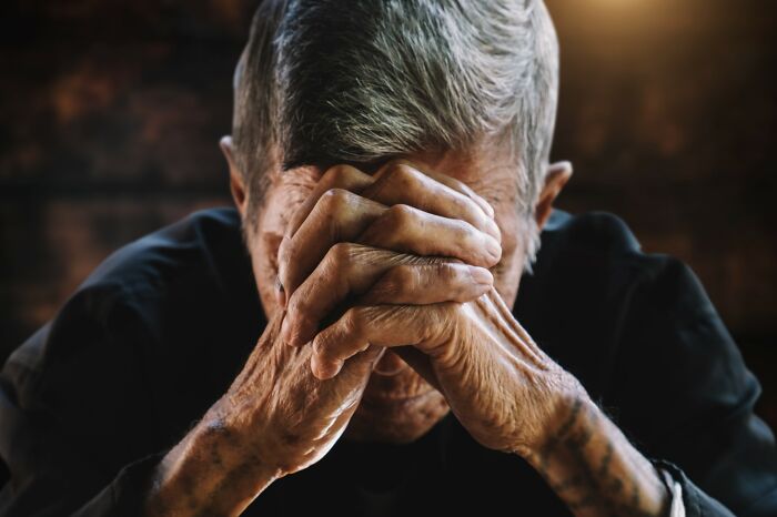 Elderly person with clasped hands and bowed head showing the emotional impact of falling for scams and their effects.