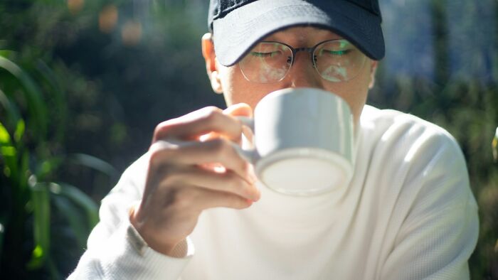 Man in glasses and cap drinking from a mug outdoors, capturing kids doing something weird passed down from their parents.