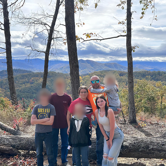 Family posing outdoors in a forested mountain area, related to father of teen slain on cruise and babysitter affair allegations.