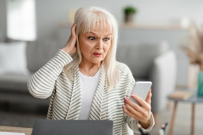 Elderly woman looking shocked at her phone, representing people who fell for scams and their effects.