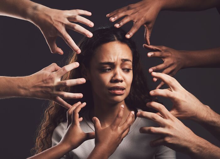 Young woman looking distressed surrounded by multiple hands reaching toward her, illustrating internet rabbit holes impact.