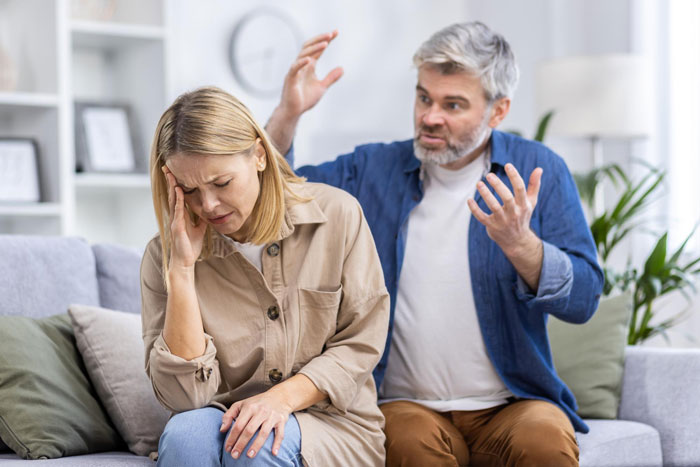 Woman called poor by stepdad arguing with him while she looks distressed on a couch in a home setting