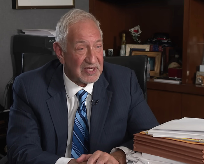 Man in a suit and striped tie speaking in an office, surrounded by folders and papers, discussing Michael Jackson allegations.