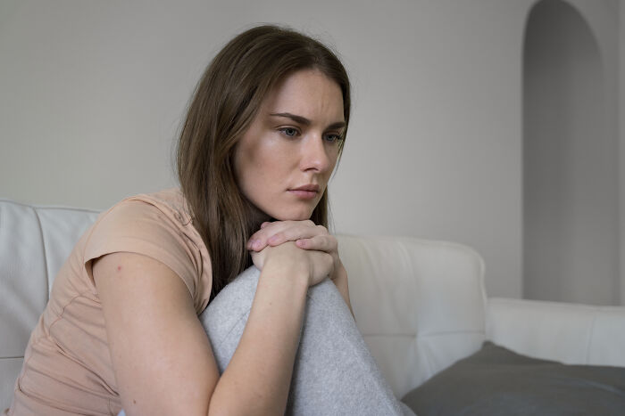 Woman with a thoughtful expression sitting on a couch, reflecting on experiences only adopted people understand.