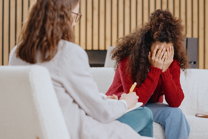 Woman with curly hair distressed and covering face during counseling session about cheating while wife is pregnant and postpartum.