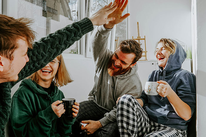 Group of friends enjoying coffee and sharing a high-five during a casual college experience indoors.