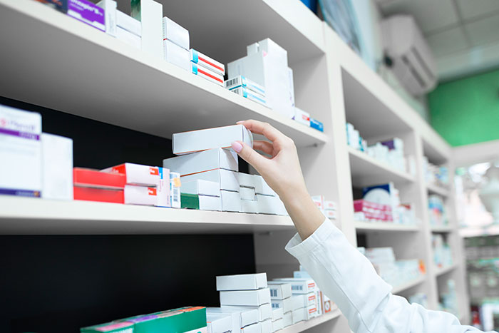 Pharmacy shelves stocked with medications and a hand reaching to pick a box, reflecting aspects of the college experience American.