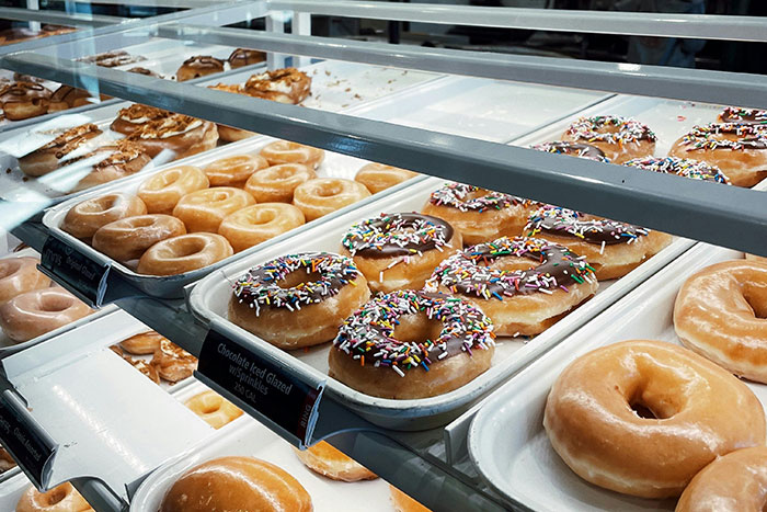 Glass display case filled with glazed and chocolate frosted donuts with sprinkles, a classic college experience snack in America.