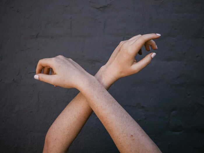 Two freckled arms crossed with hands raised against a dark wall, illustrating comically absurd facts concept.