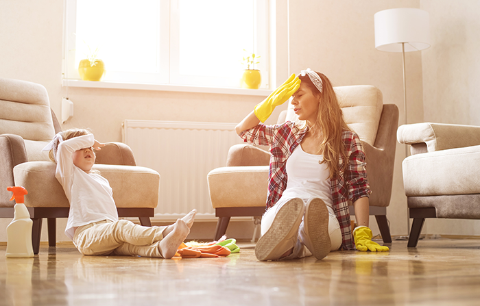 Woman and child sitting tired on floor surrounded by cleaning supplies, illustrating free babysitting on demand and sibling conflict.