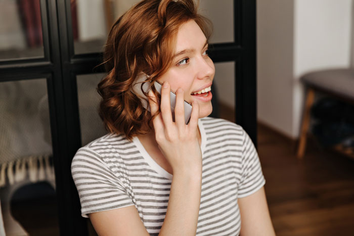 Young woman smiling and talking on phone at home, reflecting stay-at-home mom clapping back about college degree usage.