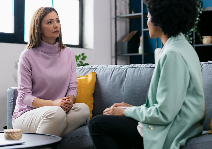 Two women having a serious conversation on a couch about charity and Christmas presents in a cozy living room.
