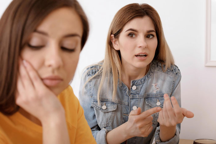 Two women in a tense conversation, one visibly upset and the other appearing frustrated, reflecting conflict over a chair.
