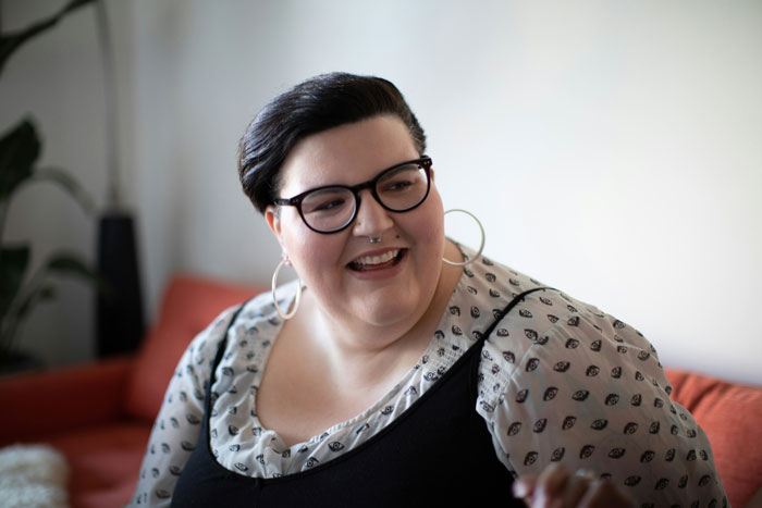 Plus size woman with glasses and hoop earrings smiling indoors, relating to obese lady and fat outburst story.