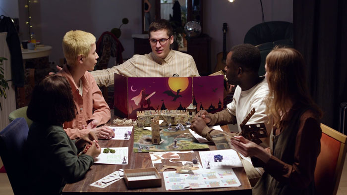 Group of friends playing a board game around a table in a cozy room, focused on strategy and dice rolls.