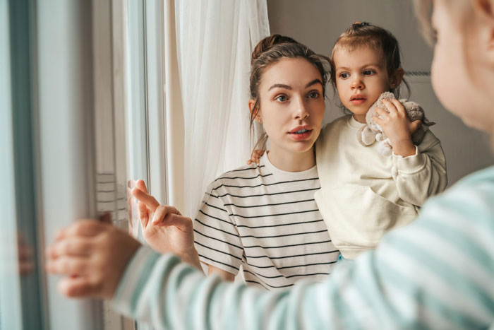 Young sister practicing gentle parenting at home, holding toddler and calmly talking near window in cozy house.