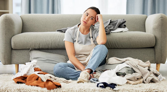 Woman sitting on floor surrounded by laundry, looking frustrated about cleaning and pest issues after sister moved in.