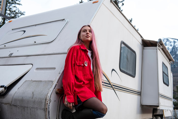 Woman with pink hair leaning against an old camper, representing woman wanting to charge sis clean-up fee after spotting roaches.