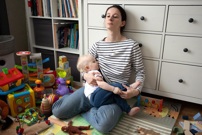Woman sitting on floor holding baby in a cluttered room, expressing concern after spotting roaches following sister's move-in.
