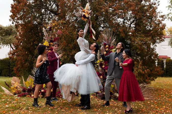 Bride lifted by groom celebrating with friends outdoors, reflecting sister wedding money culture and joyful autumn atmosphere.