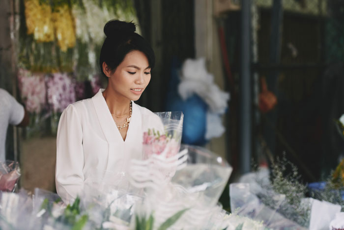 Young woman arranging flowers at market stall, reflecting sister wedding money culture and traditional customs.